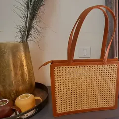 Our modern cane and vegan leather handbag, elegantly styled in a contemporary home setting. This structured bag combines traditional weaving with a sleek, professional design, making it a perfect accessory for the eco-conscious professional.