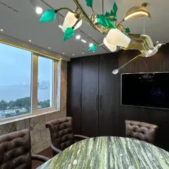 The details make the design. This custom chandelier, featuring brass birds and green glass leaves, adds a touch of nature-inspired artistry to a corporate conference room, beautifully contrasting with the dark wood paneling.