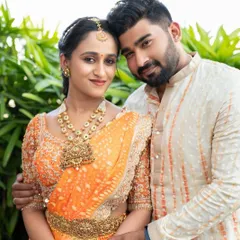 A happy couple in their coordinated outfits. The groom's cream bandhgala features subtle orange detailing, a perfect match for the bride's vibrant orange lehenga, creating a picture perfect pair.