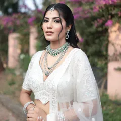 This model showcases a stunning layered diamond necklace with emerald green accents, paired with a chic white embroidered lehenga. It's a perfect blend of traditional and modern styles.