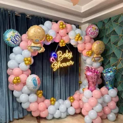 A popular 'He or She' themed baby shower decoration. This setup includes a circular balloon arch in pink and blue, with a central 'Baby Shower' neon sign and themed foil balloons.