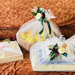 This trousseau set features a mix of fresh fruit baskets and gift boxes, all wrapped in white net with rich green and maroon ribbons. The presentation is traditional yet sophisticated.