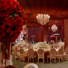 A wide view of the reception hall, blending traditional Indian opulence with modern luxury. A color palette of deep red and gold is accented with ivory florals, while dozens of chandeliers create a majestic atmosphere.