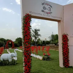 A breathtaking entrance for a romantic wedding. The grand archway with the couple's monogram leads to an aisle of red chairs and a stunning red rose arch in the distance.