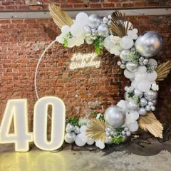 Celebrating a fabulous 40th birthday with a statement piece. This setup features a large balloon ring in silver and white, accented with dried palms and a "Happy Birthday" neon sign, all framed by marquee numbers.