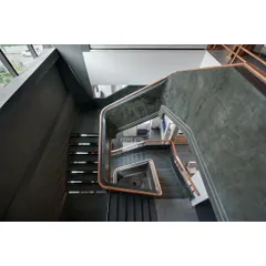 The main staircase railing is a single, sweeping curve made of ferrocement with a wooden handrail. This sculptural element creates visual interest and guides visitors physically and visually through the multi-level space.