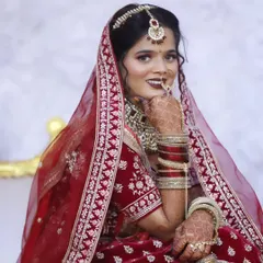 A stunning close-up of the bride in her red velvet lehenga and intricate jewelry. The makeup is bold yet elegant, perfect for a North Indian wedding.