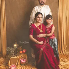 A regal family portrait celebrating a traditional Indian maternity journey. The mother, father, and daughter are dressed in elegant ethnic wear, surrounded by cultural props like brass vessels and lotuses, creating a timeless memory.