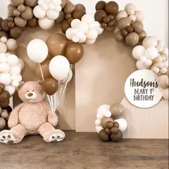 A minimalist and modern teddy bear first birthday theme. This "Hudson's Beary 1st Birthday" setup uses a neutral palette of brown and white balloons with a large teddy bear.