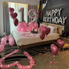 We do birthday surprises too! This 19th birthday room decoration features pink and silver number balloons, heart-shaped foil balloons, and flower petal hearts on the bed.