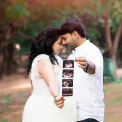 An intimate outdoor portrait of an expecting couple, touching foreheads in a moment of quiet connection. The father-to-be holds up the first glimpse of their baby: a strip of sonogram photos, symbolizing the start of their family journey.