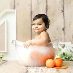 A sweet smile from a baby girl enjoying her orange-themed milk bath, a popular choice for first birthday sessions.