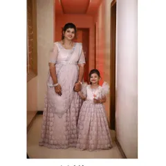 This mother and daughter are ready for a wedding in their matching pale pink outfits. The mother wears a lehenga-saree style gown, and her daughter has a matching frock with ruffled sleeves.