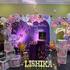 A beautiful butterfly theme designed for a cozy living room celebration. This setup includes a custom purple backdrop, a delicate balloon arch with silver accents, and illuminated letters spelling the name 'Lishika'.