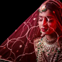 A creative bridal portrait using a red veil to create a powerful, artistic effect. The bold color and soft light emphasize the bride's features and the richness of her traditional wedding attire.
