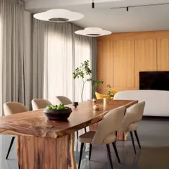 The dining area at the Amaiti Farmhouse features a stunning live-edge wood table. It acts as a natural, sculptural centerpiece, complemented by modern upholstered chairs and minimalist pendant lights that keep the focus on the view outside.