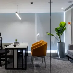 A private cabin within the open office, enclosed by glass to maintain visual connectivity. The pop of color from the visitor's chair adds personality to the professional setting.