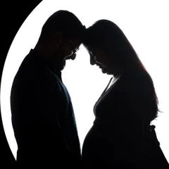 An intimate silhouette portrait of an expecting couple, their foreheads touching in a moment of quiet connection. This artistic maternity photo uses backlighting to create a beautiful, high-contrast image that focuses on their bond and the shape of the baby bump.