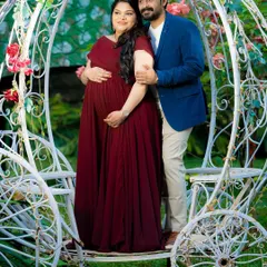 A romantic portrait of an expecting couple in a Cinderella-style carriage. The rich color of the maternity gown stands out beautifully against the white, ornate prop.