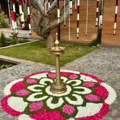 A beautiful flower rangoli (pookalam) with a traditional brass lamp at its center, a classic element for welcoming guests to a South Indian event.