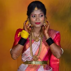 A traditional bridal portrait. This bride is adorned in classic temple jewelry, a bright red lip, and makeup that accentuates her features against a vibrant studio backdrop.