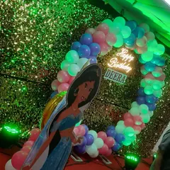 A Disney princess theme for a birthday party, featuring a Jasmine cutout against a sequin backdrop. The circular balloon arch with a "Happy Birthday" neon sign adds a magical touch.