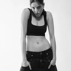 A raw, intense portrait. In black and white, with no distractions, the focus is entirely on the model's expression and body language. The high-key lighting blows out the background, isolating her form and creating a powerful, graphic image.