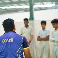 A coach addresses a group of young players in the nets. These moments of direct feedback, whether advice or a stern talk, are crucial for development.