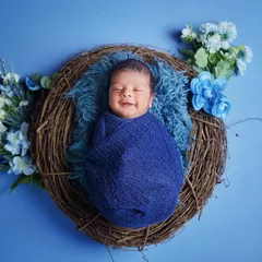 Capturing that perfect, sleepy newborn smile is my specialty. For this shot, I used a cozy nest prop with a vibrant blue theme, complete with floral accents, to create a peaceful and visually striking portrait.