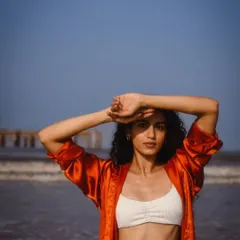 A simple, direct portrait against the sea and sky. The pose is natural, shielding her eyes from the sun, which makes it feel very relatable.