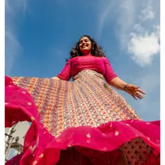 A low-angle shot capturing the bride's vibrant personality and the beautiful flare of her lehenga against a bright blue sky. A moment of pure, uninhibited joy.