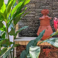 A traditional terracotta statue is nestled among lush green foliage against a stacked stone wall. I enjoy incorporating art and personal objects into the garden to create unique focal points.