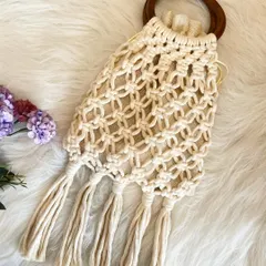 This elegant bag features a dark circular wooden handle and a beautiful net-style knot pattern. The long fringe at the bottom adds a classic bohemian touch.