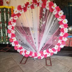 This elegant circular backdrop for Ganapati features a fan of white and pink sheer fabric, bordered with beautiful pink and white artificial flowers. It's a soft and pretty option for your home mandap.
