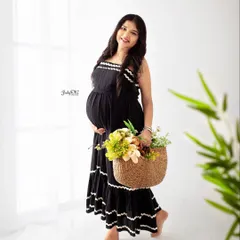A bright and airy solo portrait. The simple black dress and a basket of flowers against the white background create a fresh, happy, and casual maternity photo.
