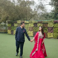 A happy couple walks hand-in-hand across a lush green lawn during their Roka ceremony, sharing a look of love.