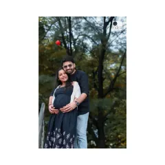 A classic couple's pose during their park maternity shoot, with the father-to-be embracing his partner from behind, both cradling the baby bump.