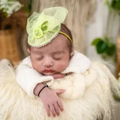 A close-up on the baby's peaceful face, highlighting the delicate features and the cute lime green fascinator. The soft, furry texture below adds to the cozy, natural vibe.