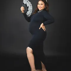 A powerful and dramatic solo portrait. The mom-to-be poses with a fan against a solid black background, creating a look of confidence and style.