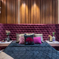 Comfort and style in every corner. This bedroom in the Filigree House features a dramatic, deep purple tufted headboard set against a warm wood-paneled wall, creating a cozy and sophisticated haven.