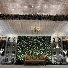 A detailed shot of the magnificent Nikaah or Walima stage. The design features a dense wall of white flowers, framed by elegant white drapes and beautiful chandeliers.