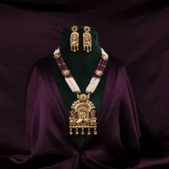 An opulent traditional Indian necklace and earring set, professionally displayed on a bust against a rich, dark purple satin background to highlight the intricate gold work and gemstones.