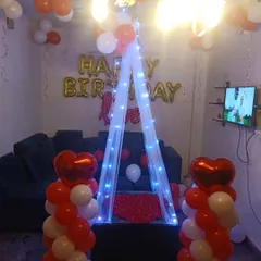 A romantic birthday surprise setup for a loved one. The canopy with fairy lights, heart-shaped balloons, and rose petals creates a very special and intimate atmosphere.