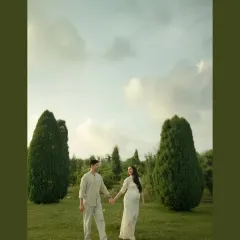 A walk to remember. This wide shot captures the couple in a beautiful, open landscape, holding hands as they begin their journey into parenthood. The composition emphasizes the start of a new adventure together.