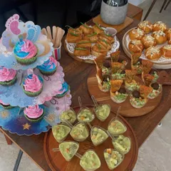 A savory spread for a baby shower, including gender-reveal cupcakes, mini quiches, Korean buns, and avocado mousse cups.