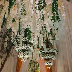 Looking up into a magnificent ceiling installation of hanging white wisteria and chandeliers made from rings of white carnations.