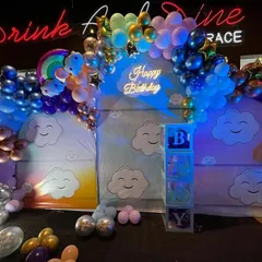A dreamy sky-themed birthday party. This backdrop features cute smiling clouds, a colorful balloon arch, a light-up number '1', and transparent 'BABY' boxes.