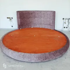 A special request for a custom-made round bed. This unique piece is fully upholstered in a textured fabric and is built on a strong wooden base.