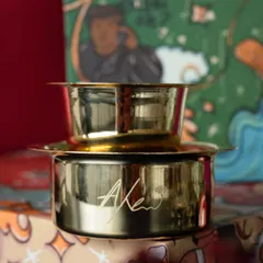 A close-up of the personalized coffee filter included in the wedding return hamper. The couple's initials are elegantly engraved on the brass, adding a touch of class.