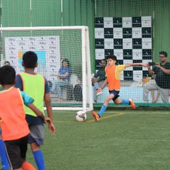A player takes a shot on goal during a tournament match, with parents watching and cheering from the sidelines.
